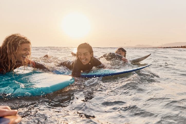 Dos alumnas remando sobre sus tablas de surf al atardecer