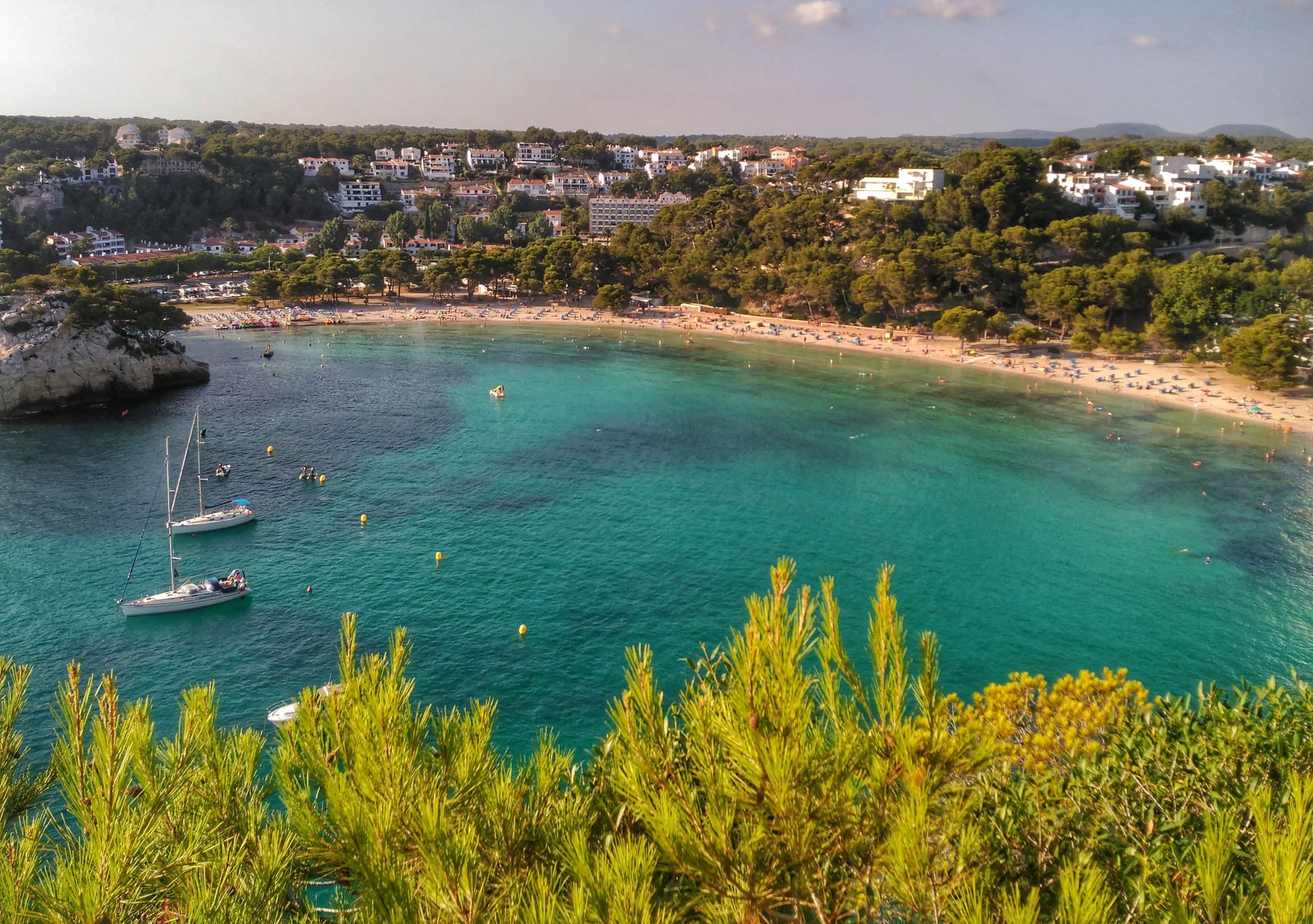 Cala Galdana vista desde el pinar, con la playa al fondo de la ensenada y veleros fondeados en agua turquesa